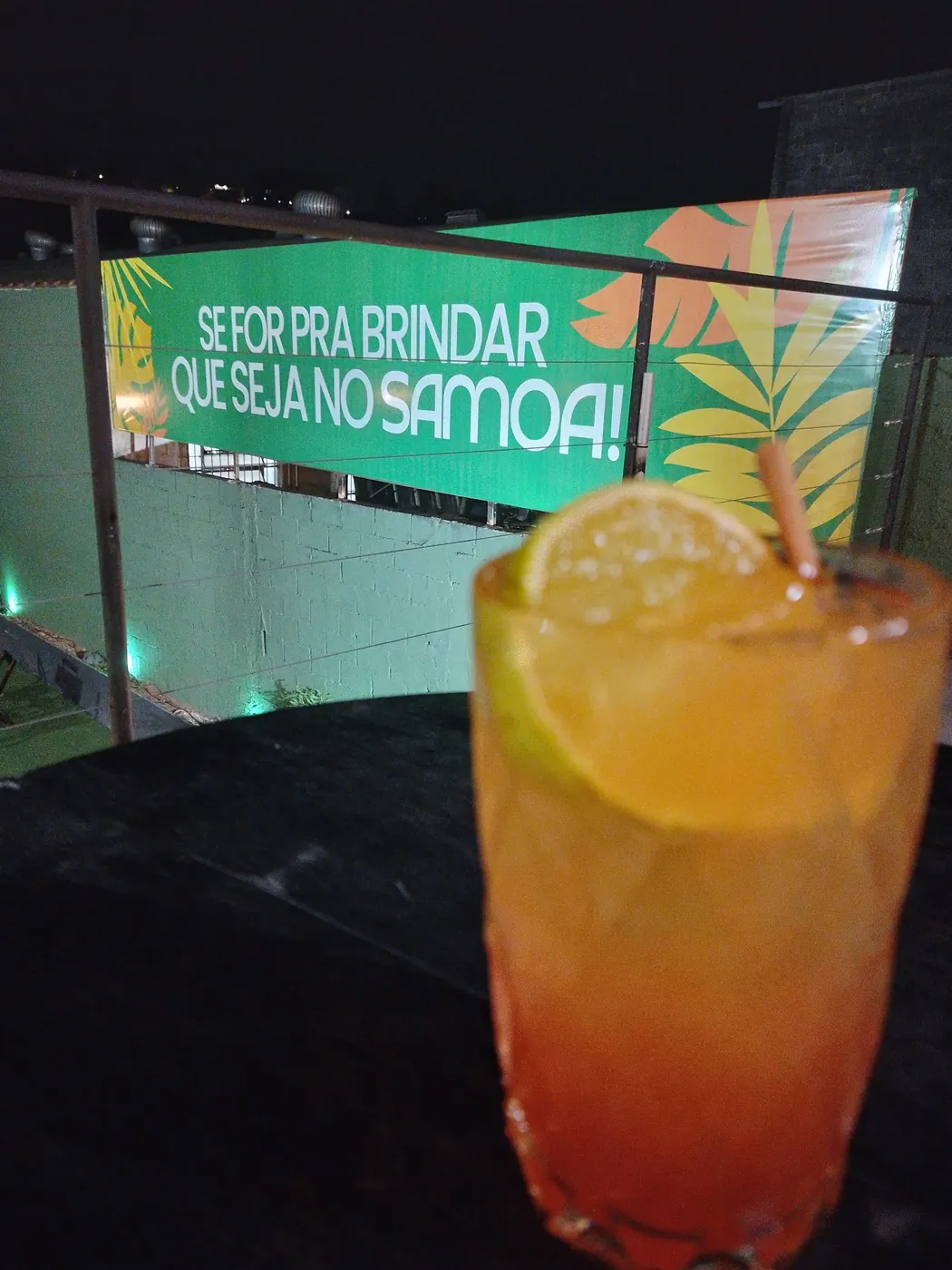 Drink cítrico em frente ao painel “Se for pra brindar, que seja no Samoa!”